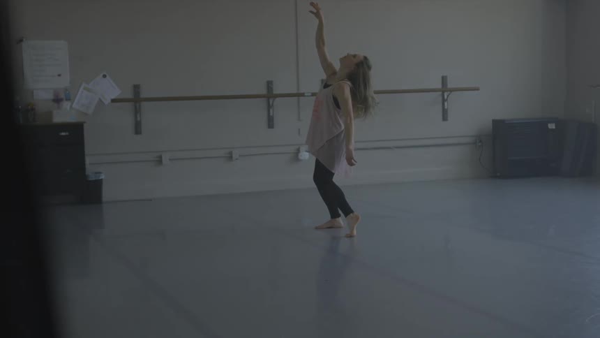 A woman dances alone in a dance studio during the day