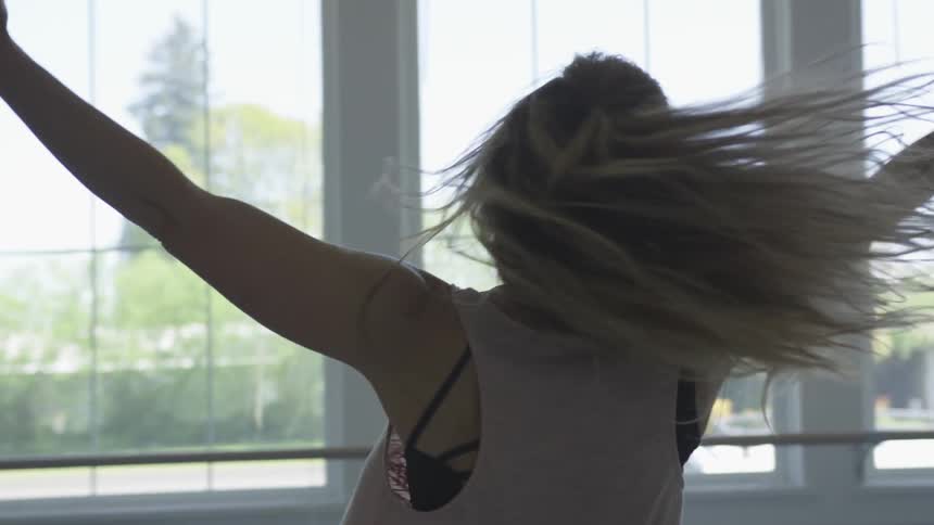 A young woman performs a spinning dance maneuver in a dance studio during the day
