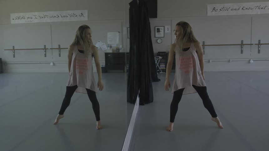 Young woman dancing in a studio looks at her reflection in a wall mirror