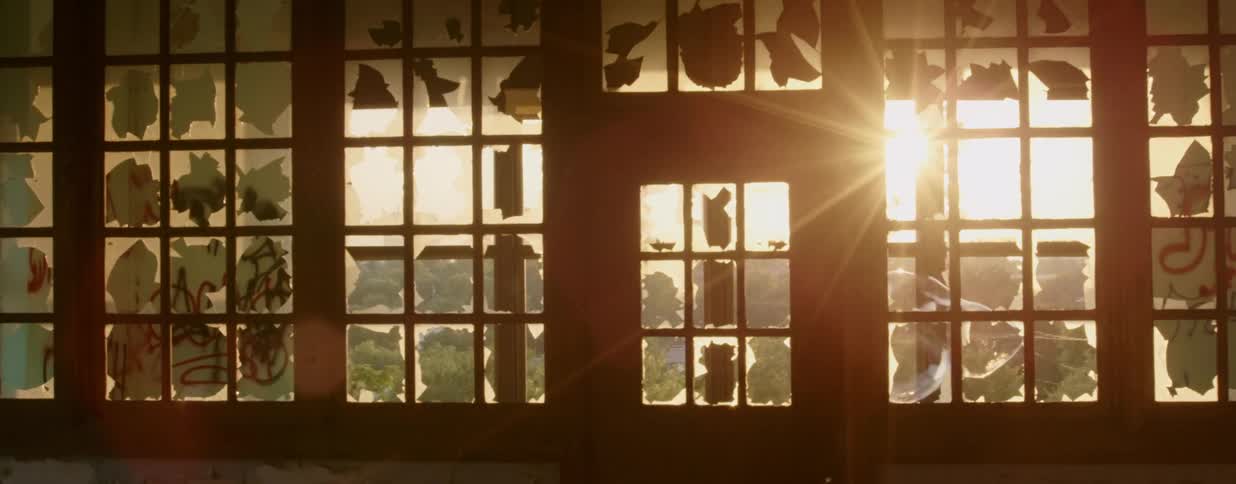 Windows in a dilapidated building are broken and marked with graffiti