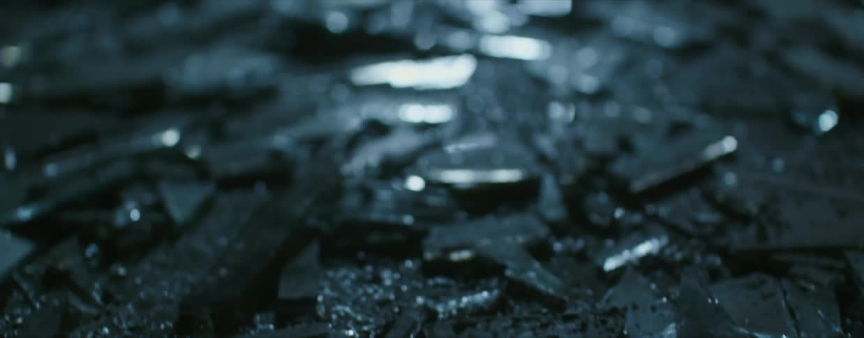 A close view of broken glass and shards on a concrete floor in a shadowy room
