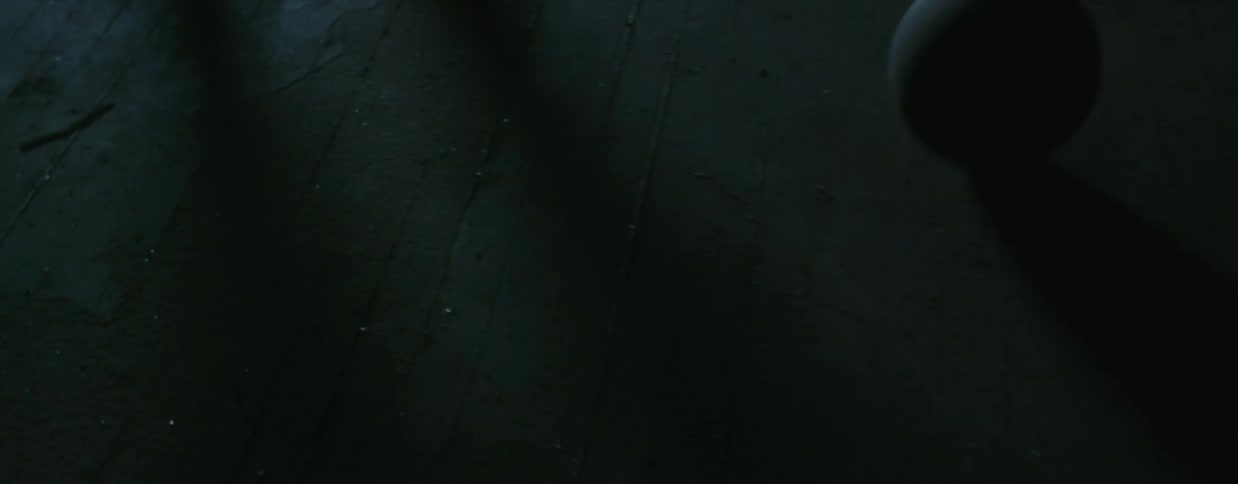 In a darkened room a person gently kicks a lopsided ball over the floorboards