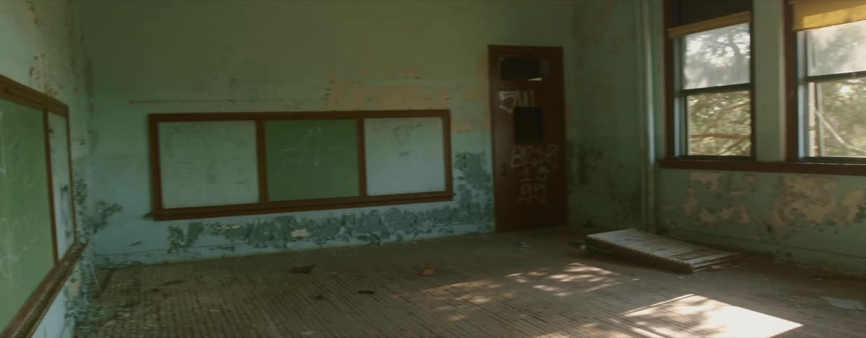 Sunlight shines through a row of windows into a decrepit classroom in an abandoned school
