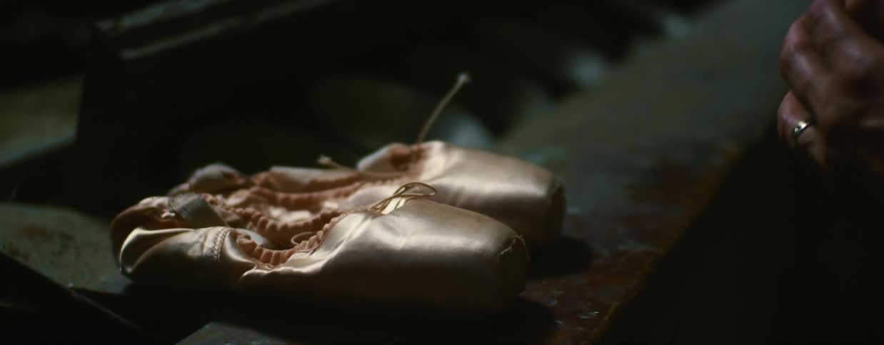 Worried looking older woman sets ballet slippers on dusty counter and looks up