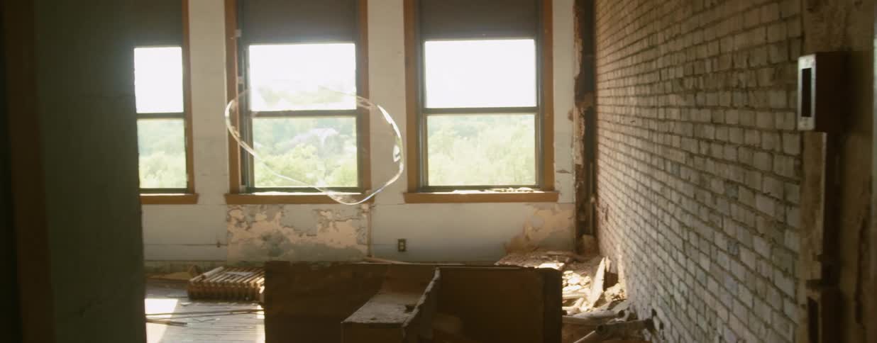 A large bubble contorts as it floats in a room in a ruined building before suddenly bursting