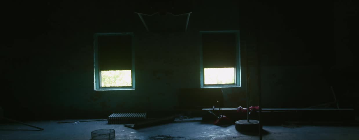Sun coming through two small windows provides the only light for a large empty room in a building