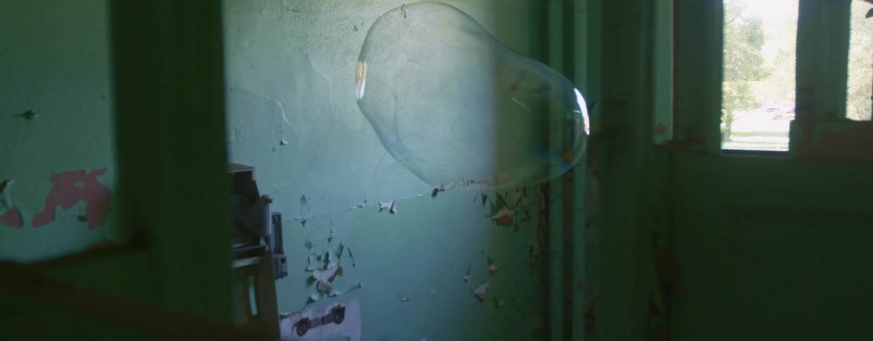A bubble in a building with peeling paint floats and then pops
