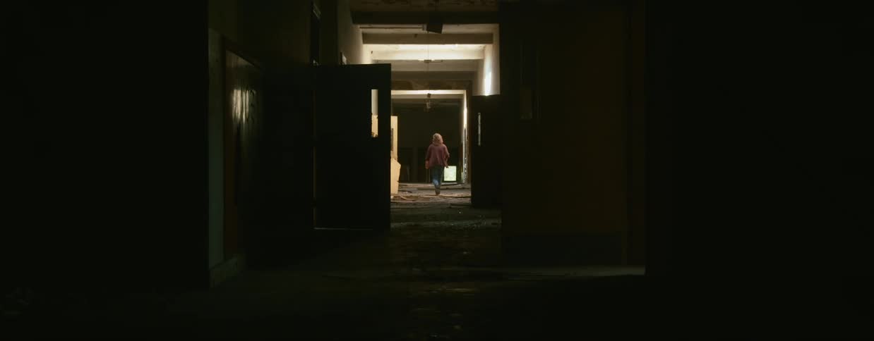 A person walks down the corridor of a derelict building during the day