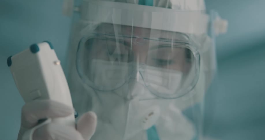 A female medical professional is covered in multiple layers of personal protective equipment while performing a procedure