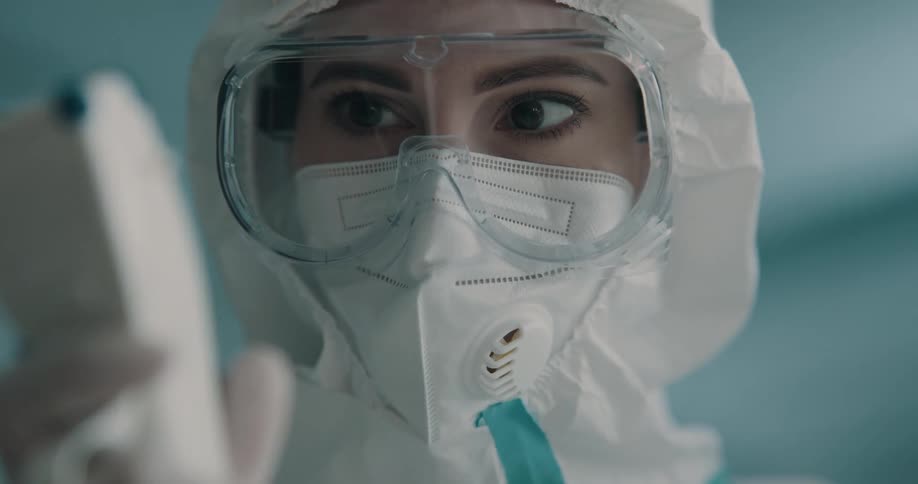 A woman working in a lab wearing protective gear looks at a medical device