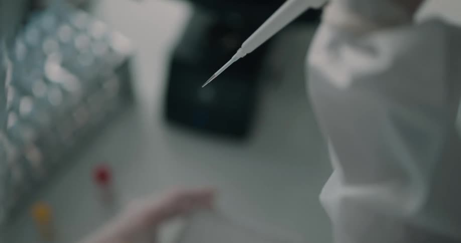 A woman in a lab uses a syringe to remove liquid from a container and put it in a tray