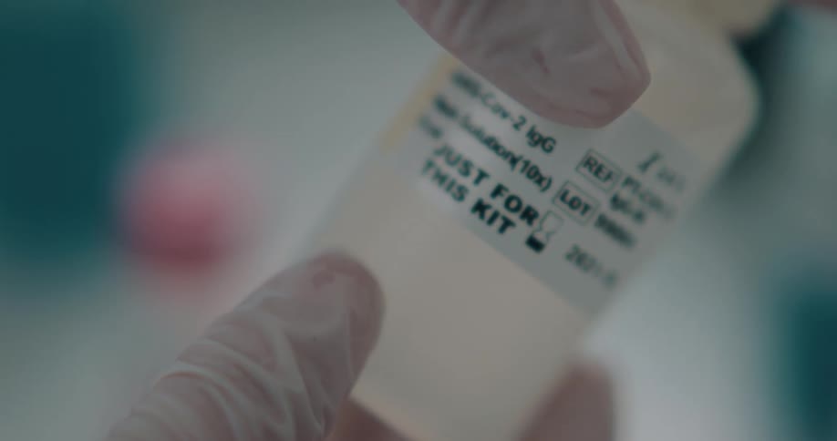 Lab technician wearing latex gloves holds a sample bottle in a laboratory