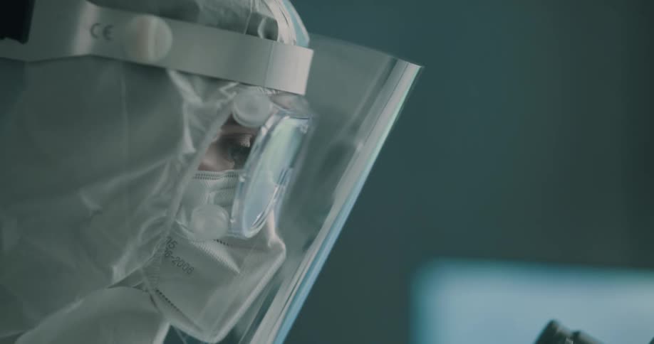 A woman in protective gear in front of a microscope