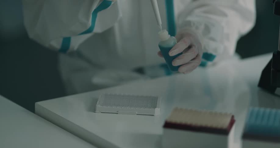 A woman in a lab uses a syringe to withdraw liquid from a bottle and put it in a tray