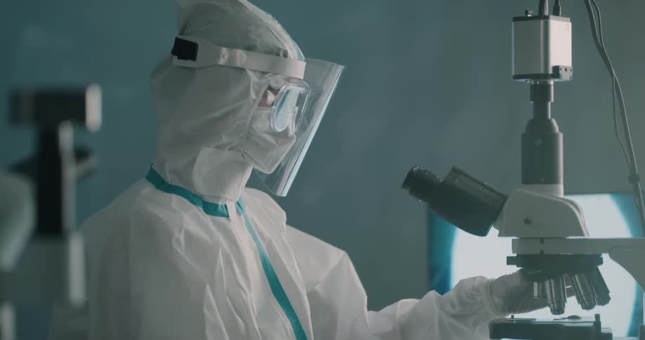 Lab technician wearing protective equipment uses a microscope on a laboratory