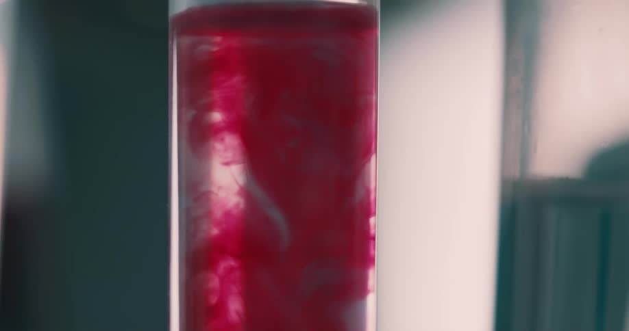 Red liquid is poured into a vial full of water