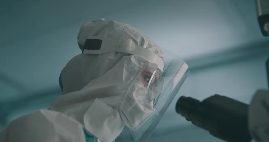 A woman in hazmat gear looks in to a microscope