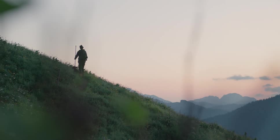 Hunter carrying a rifle walks on the hills near the mountains with his dog