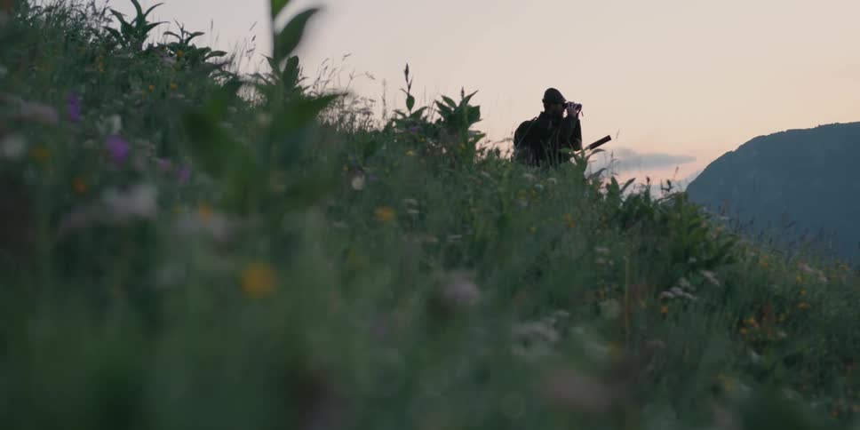 A person stands on a hill looking through binoculars