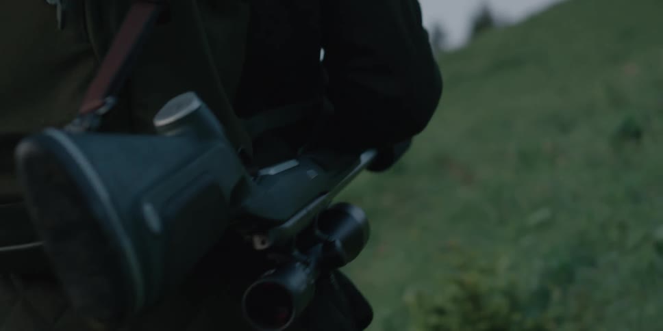 A man walks along a rural field carrying a rifle