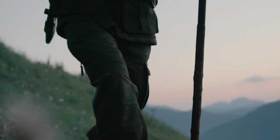 A man with binoculars a rifle and a dog hiking on a hill