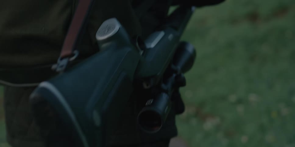 A man wearing a backpack hikes up a hill as a rifle hangs at his side