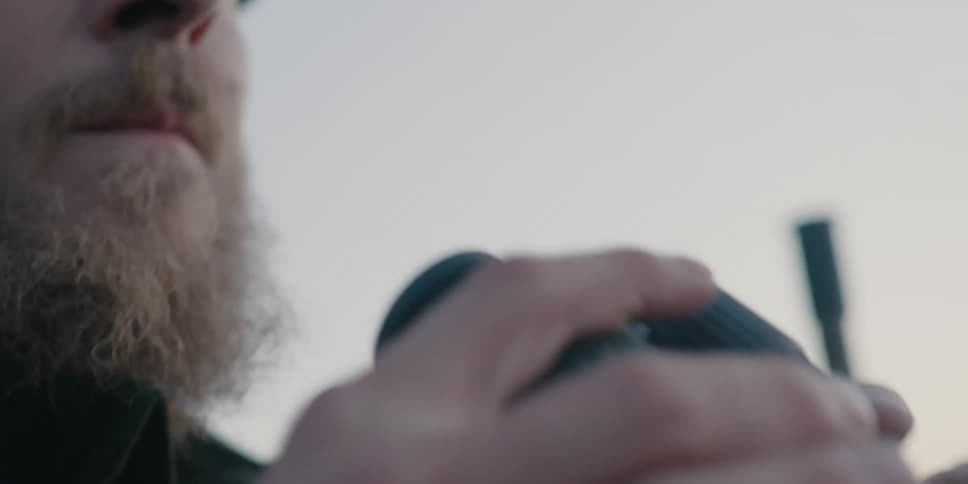 A man standing outdoors looking through his binoculars slowly lowers them from his face