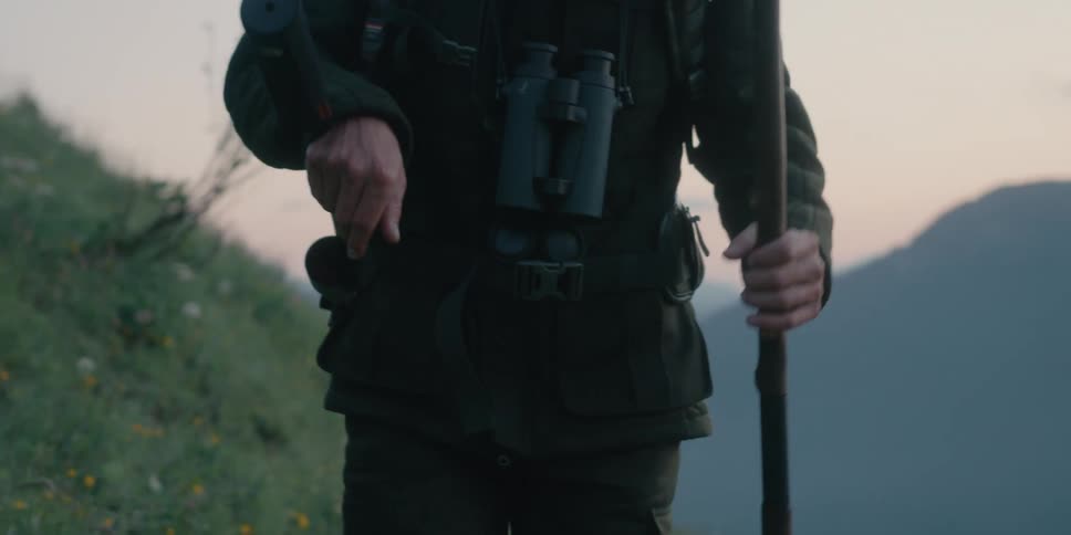 A soldier carrying a rifle in a sling walks through foggy hills during the evening