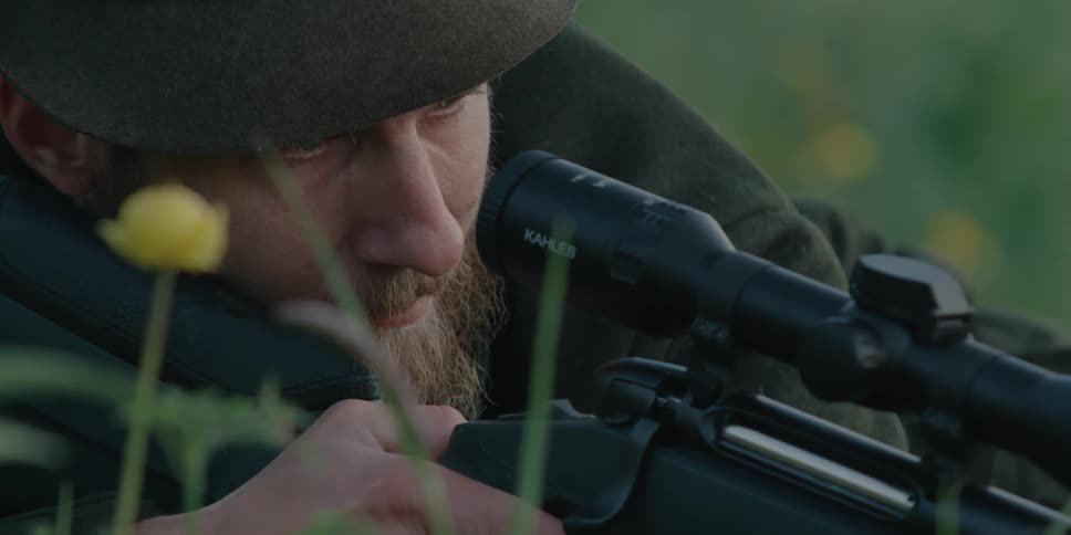 Man in field looks down sight of hunting rifle