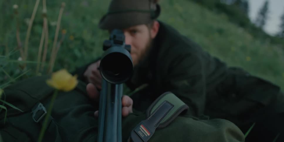 A man lays low on the ground with a weapon close to his face