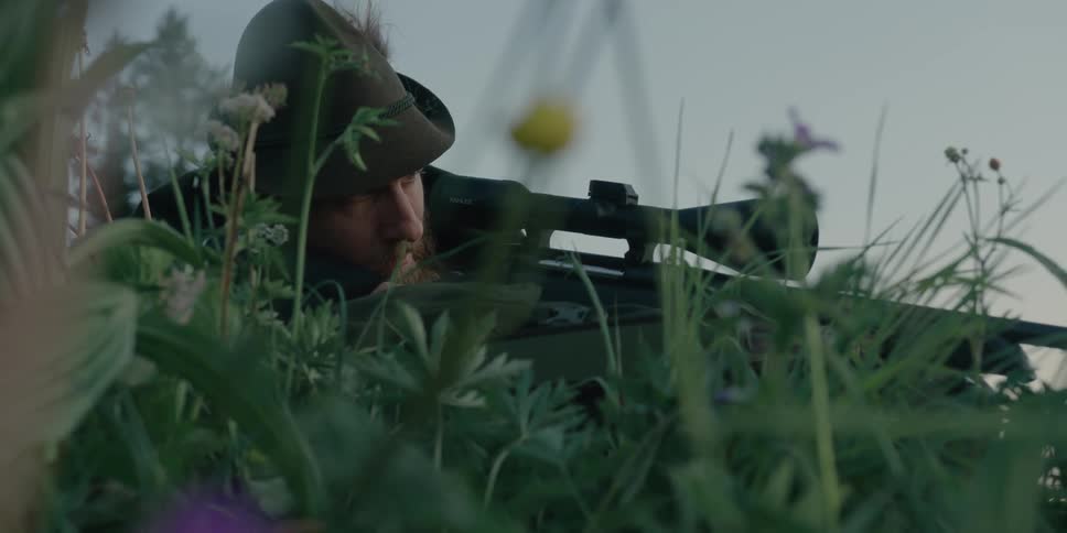 Man aims rifle lying concealed among the plants