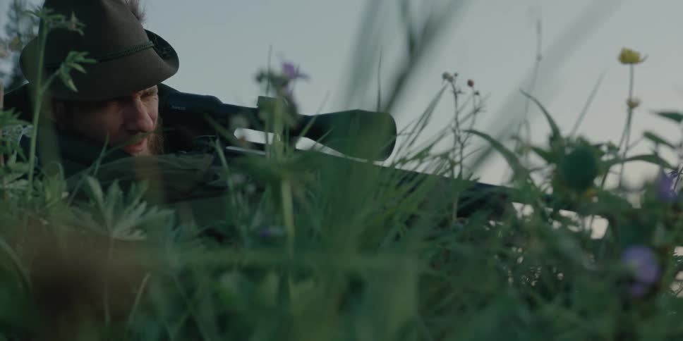Man laying in grass aims and fires hunting rifle