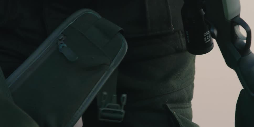 A man with a backpack binoculars and a rifle on a grassy hill