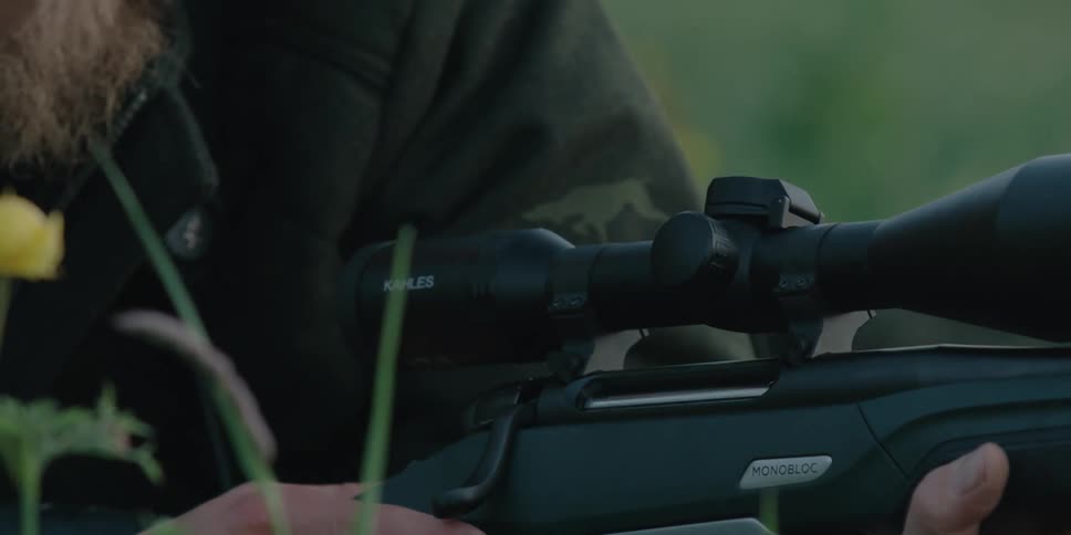 A mean lays low on the grassy rural ground with a rifle up to his face