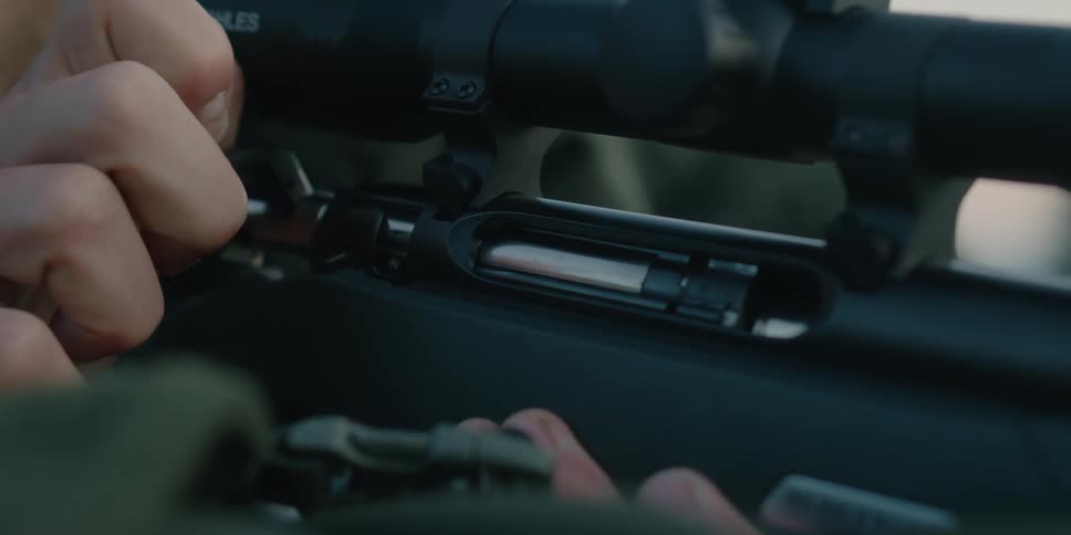 A bearded man looks through the scope of a rifle as he ejects a casing