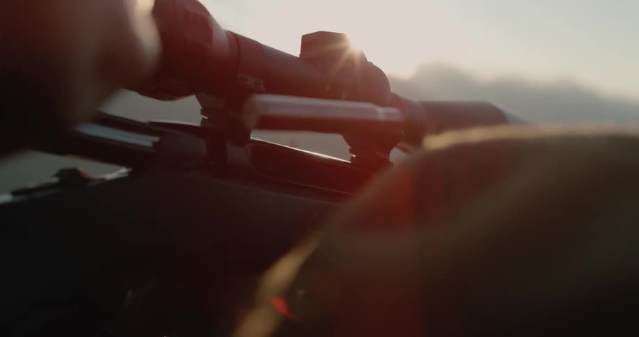 Man pulls the bolt of a rifle to eject a spent cartridge at sunset
