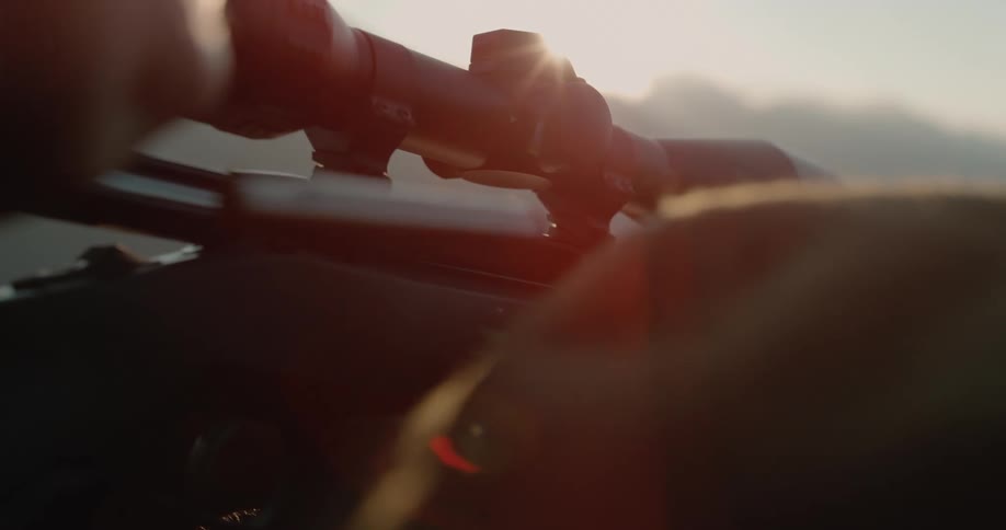 A person pulls the bolt of a sniper rifle to eject a shell at sunset