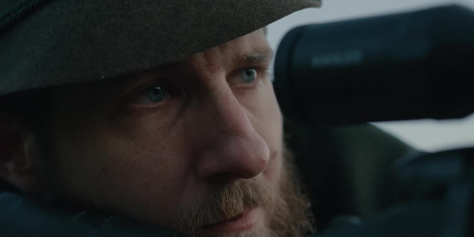 Man laying on the ground outdoors looks through the scope of a rifle