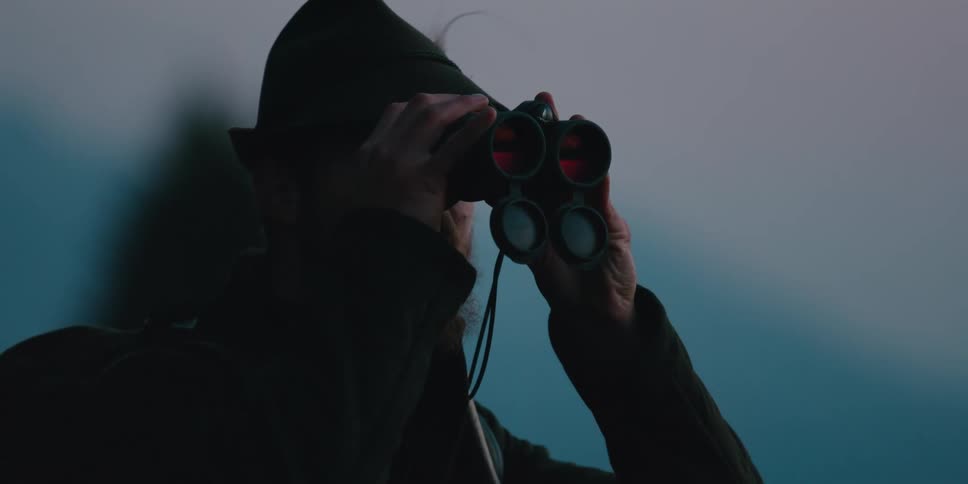 A man with a backpack and binoculars hiking with the sky in the background