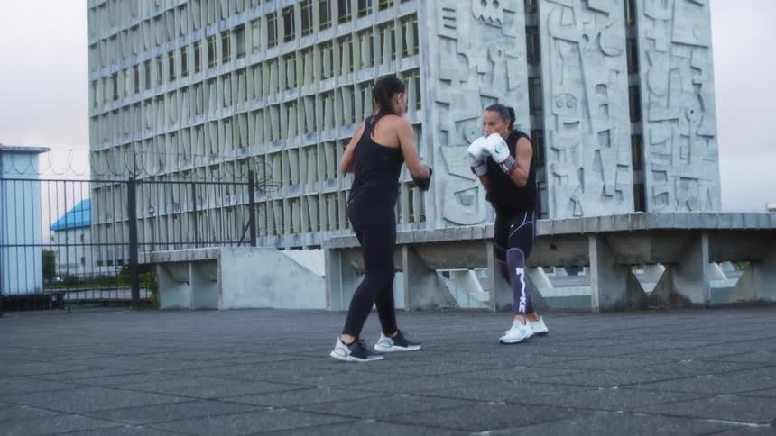 Two women spar with each other next to a large city building