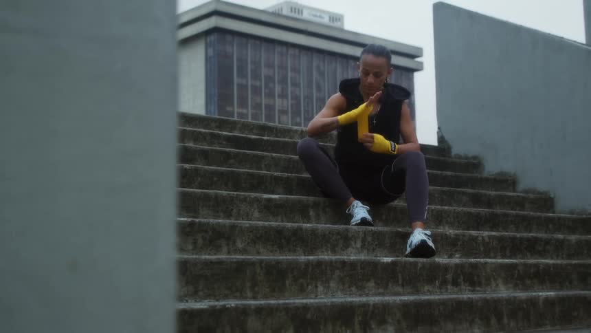 Young woman sitting in concrete stairs wraps hands with yellow wrap