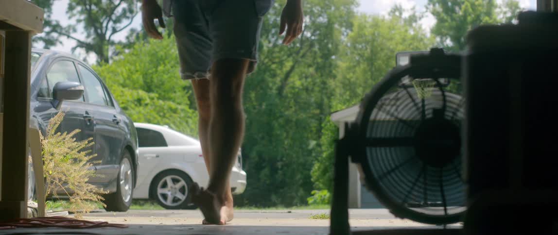 A man opening a garage door with vehicles and trees in the background