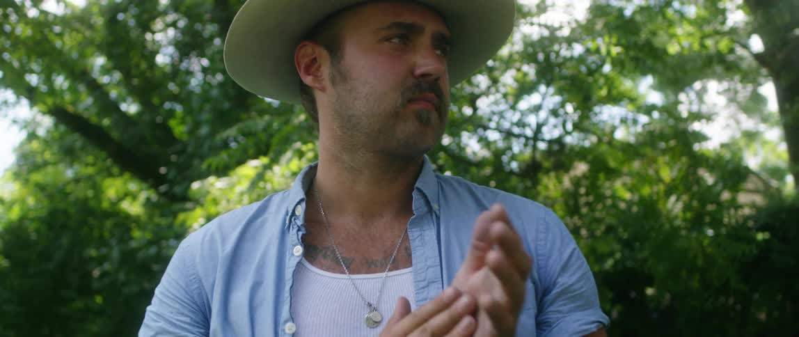 A man with a hat rubbing his hands with trees and the sky in the background
