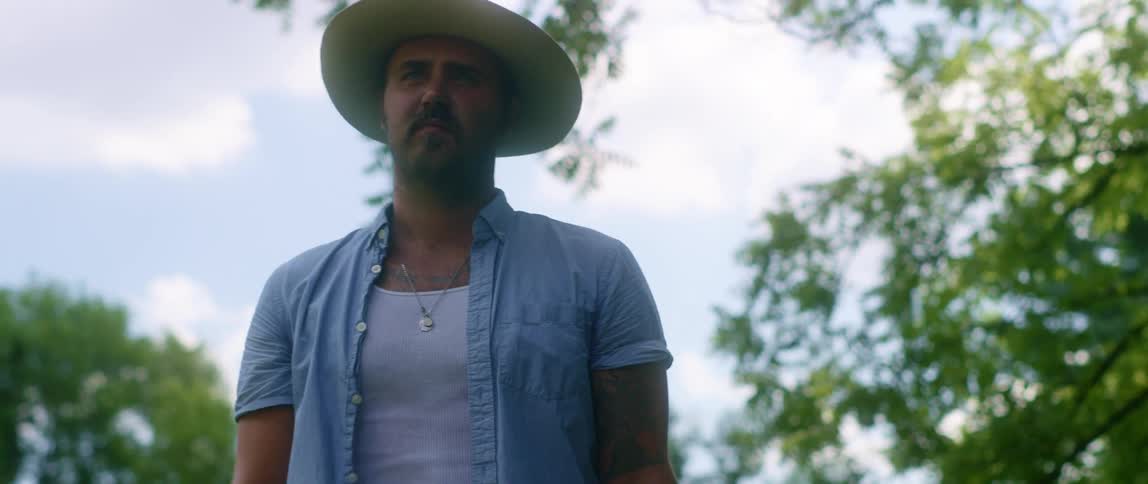 Man wearing a hat stands near the trees at day