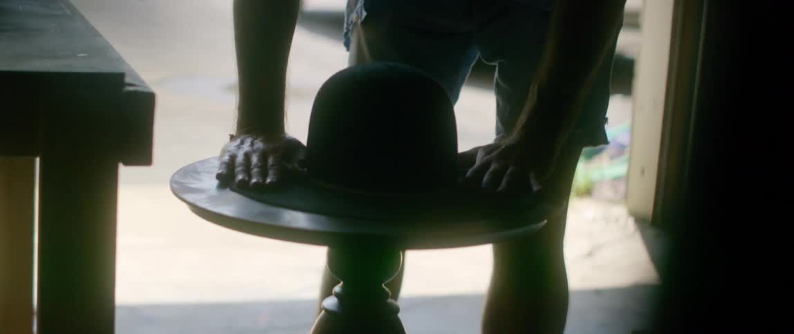A man sets a hat on a table in his garage and smooths the brim down