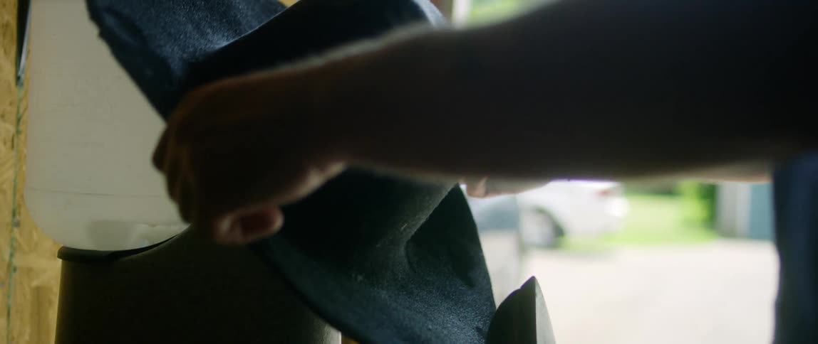 Hat maker places hat on holder near iron with car visible in background