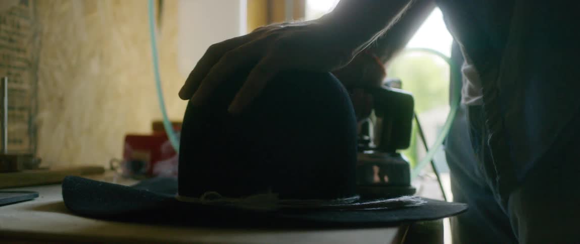 Person irons brim of felt hat on workbench