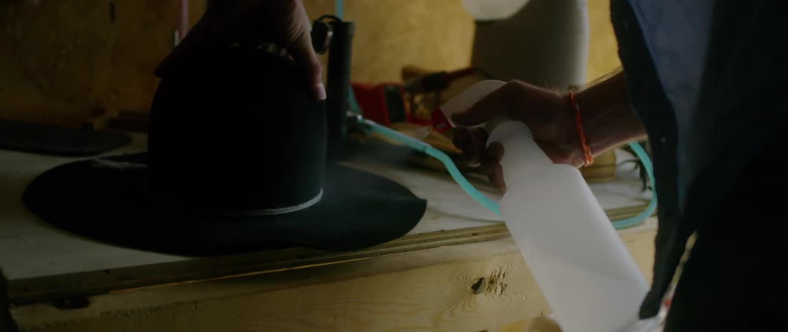 Milliner treating a hand made hat with a mist of liquid sprayed from a bottle in a workshop