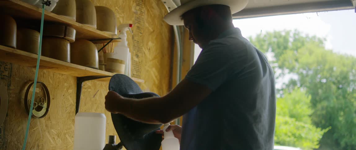 A man stands in a garage and sprays liquid on a hat