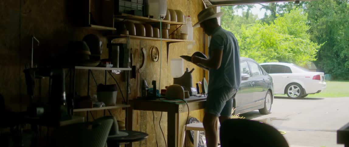 A man stands inside a garage with a hat fitter